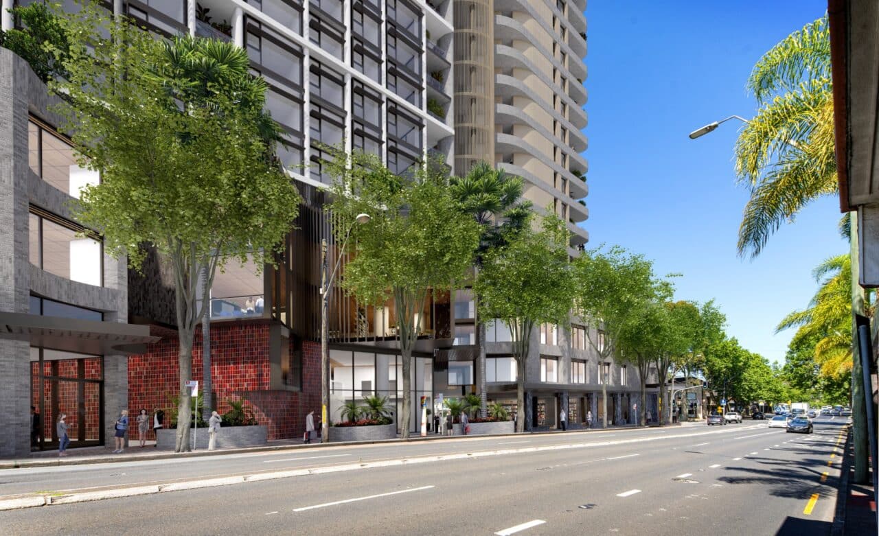 Amid the bustling Fiveways in NSW, a street view reveals a modern Falcon & Alexander high-rise building surrounded by trees. People stroll along the sidewalk beneath the clear blue sky.