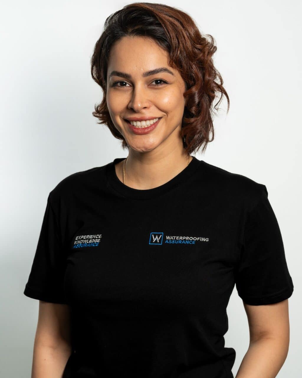 A person with short, wavy hair smiles while wearing a black T-shirt with company logos.