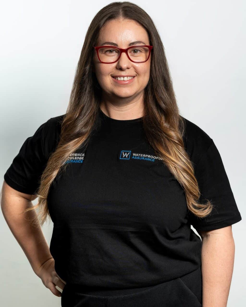 Person with long hair and red glasses, wearing a black T-shirt with logos and white text.