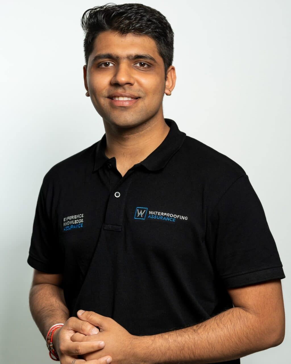 Person in a black polo shirt with company logos, standing against a plain background.