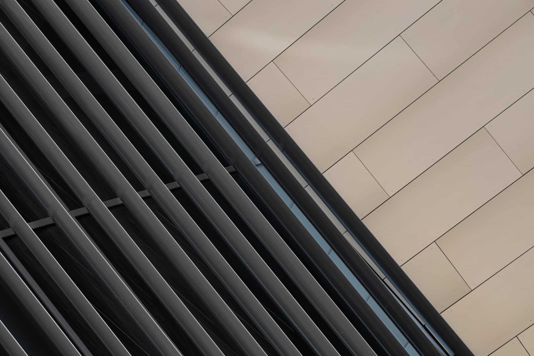 Close-up of a modern building facade with vertical metal slats on the left and light-colored horizontal panels on the right, forming a diagonal composition.